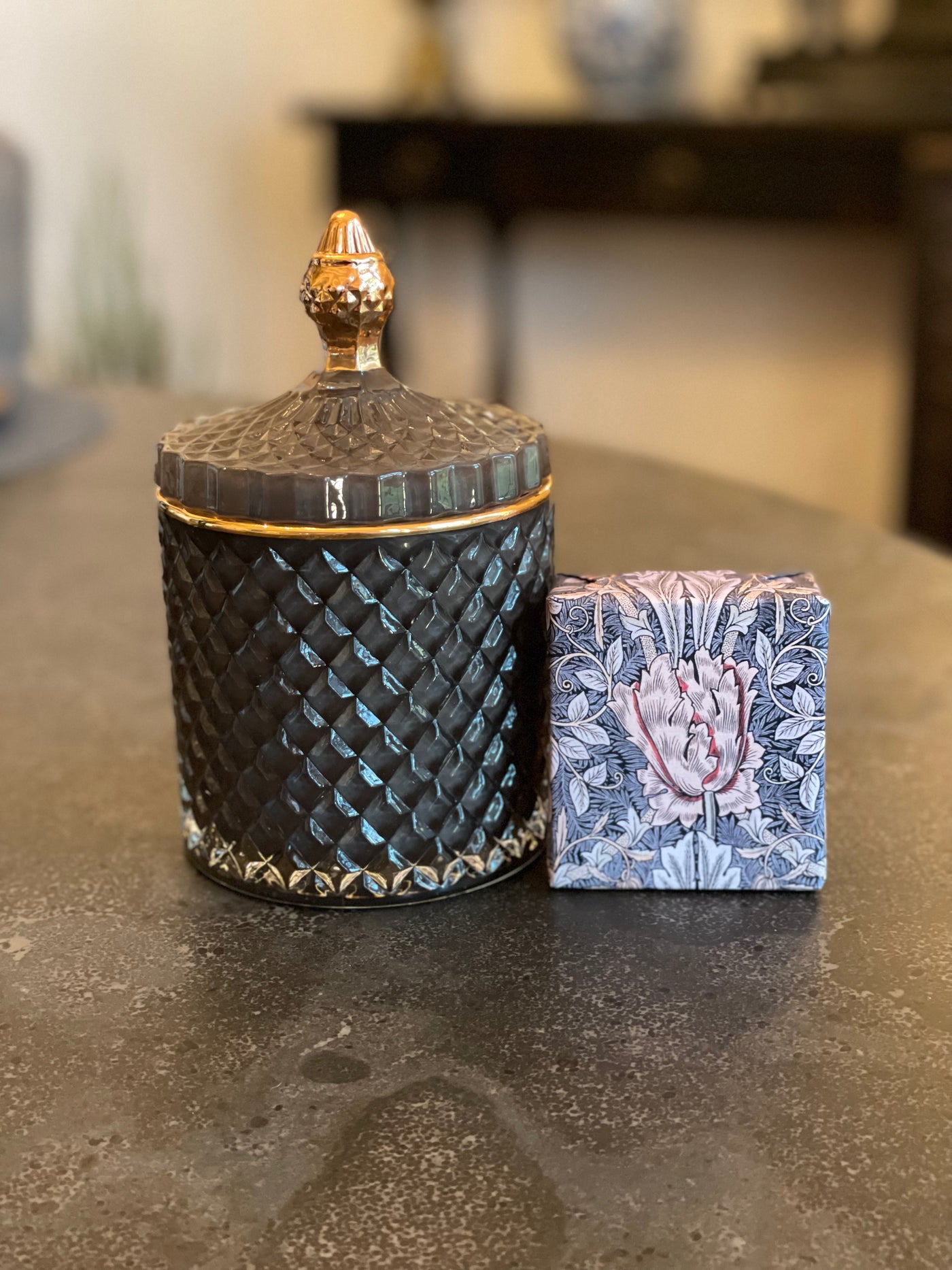 Smoky blue glass lidded vessel with gold trim displayed beside a hand-wrapped soap